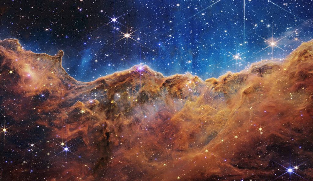  “mountains” and “valleys” speckled with glittering stars is actually the edge of a nearby, young, star-forming region called NGC 3324 in the Carina Nebula. Captured in infrared light